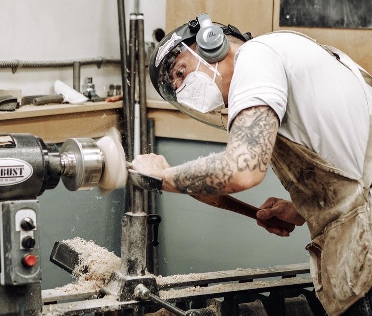 Nate with a face sheild, mask, and ear protection turning the inside of a bowl on a lathe